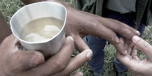 Trabalhador libertado mostra o que são condições degradantes de trabalho: a água suja que bebia, a mão machucada por falta de luvas na aplicação de pesticida, a ausência do dedo que perdeu por inexistência de equipamentos de proteção. Ficou de fora a comida estragada que era fornecida a eles e o alojamento precário (Foto: Leonardo Sakamoto)